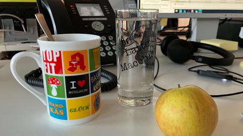 Kaffeetasse, Apfel und Wasserglas auf einem Schreibtisch mit Telefon und PC