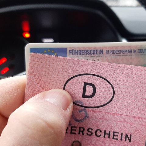 Eine Plastikkarte und ein alter rosaner Führerschein vor einem Auto-Lenkrad.