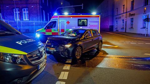 Ein Polizeiwagen, ein Auto mit kaputter Vorderseite und ein Rettungswagen stehen nachts auf einer Kreuzung.