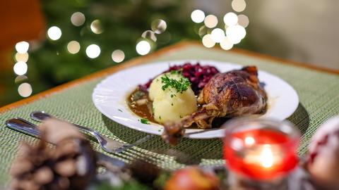 Eine Portion Gänsekeule mit Rotkraut und Klößen steht auf einem Tisch in einem Restaurant. 