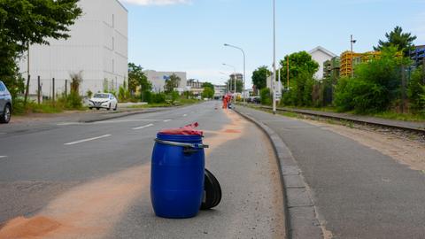 Gefahrgutaustritt in Darmstadt - eine Säuberngsspur auf der Straße, zwei Menschen mit Schutzanzügen im Hintergrund, im Vordergrund eine blaue Tonne.