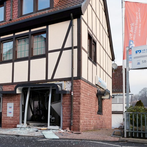 Gebäude von außen mit einem zerstörten Eingang im Erdgeschoss. Daneben Fahnen mit dem Volksbank-Logo.