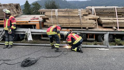 Ein Lastwagen mit Holzbrettern beladen steht in einem Baustellenbereich, die Mittelschutzplanke ist verbogen, Feuewehrkräfte schweißen