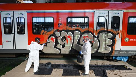 Bahnmitarbeiter in weißen Anzügen schrubben die Außenfassade einer S-Bahn. 