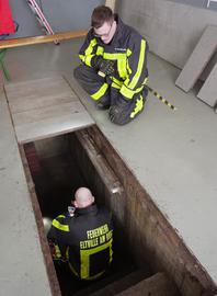 Feuerwehrleute knien vor und in einem Kellerschacht. 