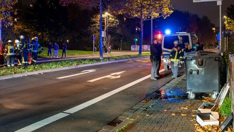 Feuerwehrleute und Polizisten an einer Straße mit Mülltonne im Vordergrund