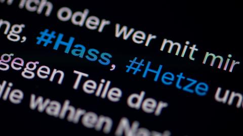 Auf dem Bildschirm eines Smartphones sieht man die Hashtags Hass und Hetze in einem Twitter-Post.