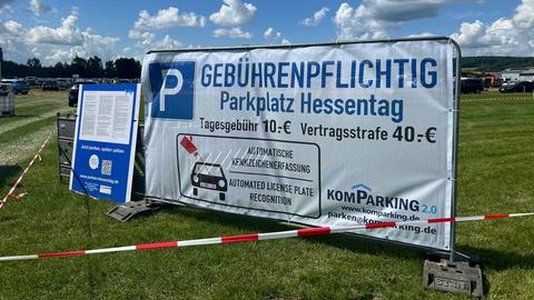 Auf dem Hessentag steht ein großes, weißes Schild auf einer Wiese. Es weist auf die Parkplatzkosten hin.