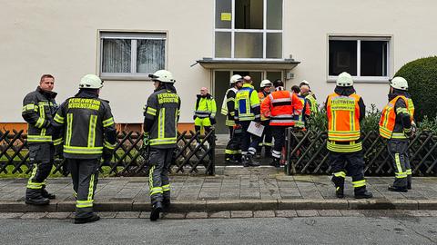 Einsatzkräfte der Feuerwehr stehen vor einem vierstöckigen Mehrfamilienhaus in Heusenstamm.