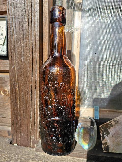 Nahaufnahme: Bierflasche aus braunem Glas. Die Flasche hat statt eines Papieretiketts ein Relief in der Glaswand, das den Schriftzug "Kronenberg" und eine Krone abbildet. 