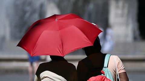 Menschen auf dem Frankfurter Opernplatz schützen sich mit einem Schirm vor der Sonne. 