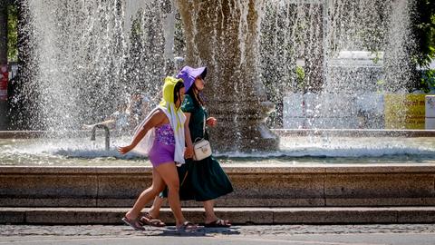 Zwei Frauen laufen mit Kopfbedeckung vor einem Brunnen an der Frankfurter Oper.