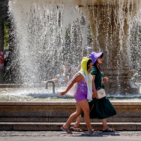 Zwei Frauen gehen mit Kopfbedeckungen vor einem Brunnen der Frankfurter Oper.