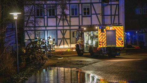 Ein Feuerwehrauto vor einem Fachwerkhaus, im Vordergrund eine große Pfütze.