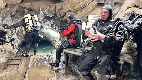 Drei Taucher sitzen vor einem Höhleneingang im Bergwerk bei Willingen