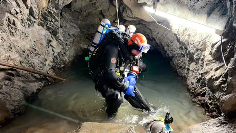 Ein Höhlentaucher steht in seiner Montur mit Gasflaschen und Helm im Höhleneingang.