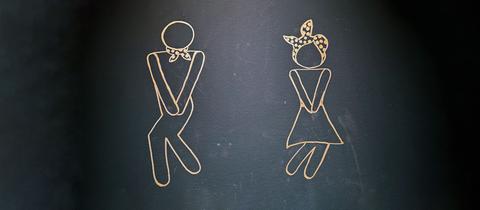Foto einer Linien-Zeichnung an einer Tafel oder schwarzen Wand: Ein Mann und eine Frau halten sich jeweils die Arme in den Schritt und die Beine sind leicht eingeknickt.