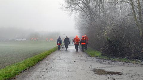 Ein Feldweg im Nebel, auf dem mehrere Personen zu erkennen sind, einige davon mit neon-orange-farbenden Jacken.