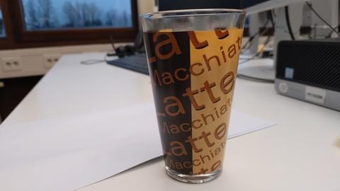 Kaffee in einem halbdurchsichtigen Glas mit mehreren Aufschriften "Latte macchiato"