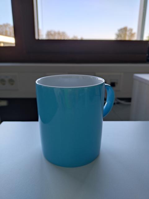 Blaue Kaffeetasse vor Fenster, dahinter blauer Himmel