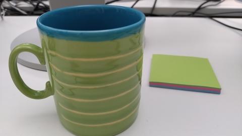 grüne Kaffeetasse mit blauem Rand neben kleinem Block mit grünen Klebezetteln