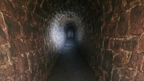 Der Strahl einer Taschenlampe beleuchtet einen aus Sandstein gebauten Abwasserkanal, der etwa 1,7 Meter hoch und 90 Zentimeter breit ist