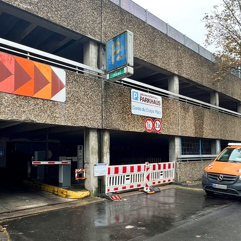 Altes Parkhausgebäude von außen. Unter dem Schild "Parkhaus" ist die Einfahrt mit rot-weißen Absperrgittern versperrt.