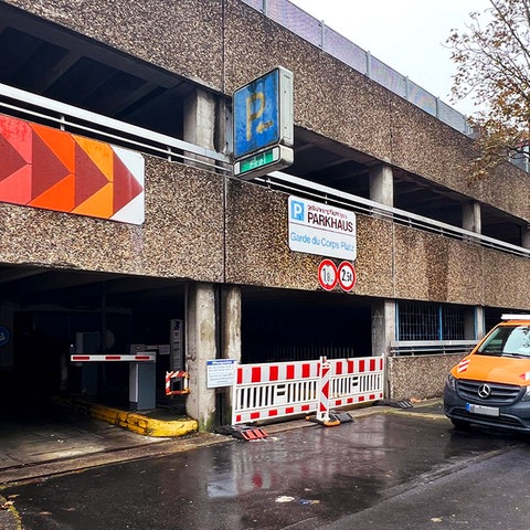 Altes Parkhausgebäude von außen. Unter dem Schild "Parkhaus" ist die Einfahrt mit rot-weißen Absperrgittern versperrt.