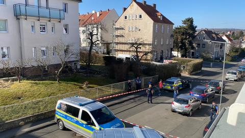 Polizeiwagen stehen auf einer Straße zwischen mehrstöckigen Wohngebäuden. Das Foto ist aus einem höher gelegenen Fenster heraus aufgenommen.