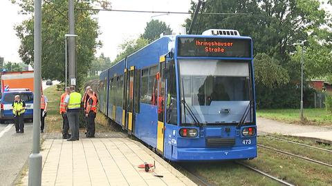 Eine Straßenbahn steht an einem Bahnsteig. Daneben Männer in neonfarbenen Schutzwesten und ein Maßband auf dem Boden.