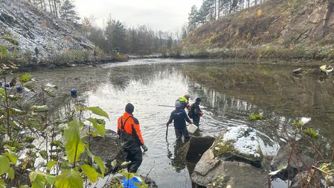 Ein See vor einem Steinbruch mit Menschen in Anglermontur im Wasser