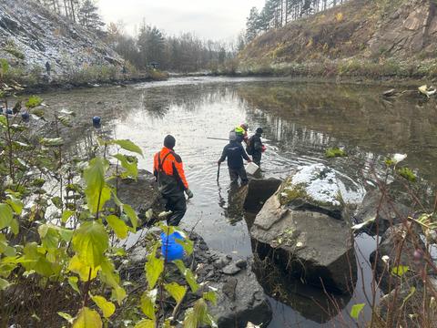 Ein See vor einem Steinbruch mit Menschen in Anglermontur im Wasser