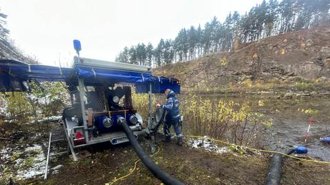 Eine große Pumpe mit dicken Schläuchen vor einem See