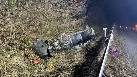 Schwarzer Pkw liegt nachts auf dem Dach im Straßengraben im Gebüsch hinter einer Leitplanke