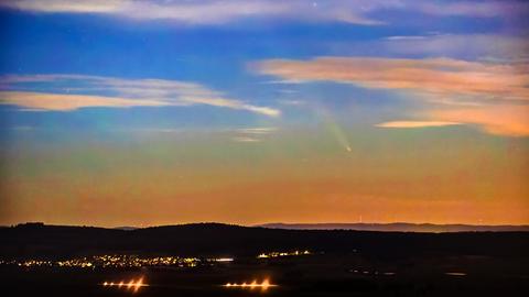 Landschaft und Himmel in der Dämmerung. Im Himmel ist zwischen Wolken ein heller Punkt zu sehen, der eine hellere Spur nach sich zieht.