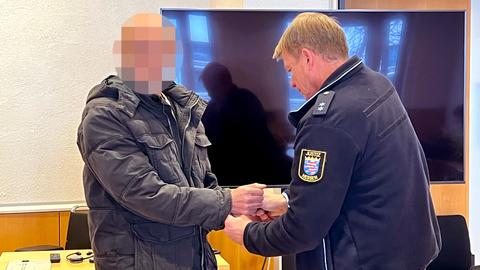 Ein Mann mit verpixeltem Gesicht hält die Hände einem Justizbeamten in Uniform entgegen, der Handschellen abnimmt.