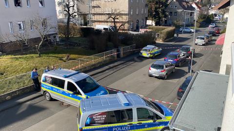 Mehrere Einsatzfahrzeuge der Polizei sperren eine Straße ab. Links steht ein Mehrfamilienhaus. Die Straße ist zusätzlich mit einem Flatterband abgesperrt. 