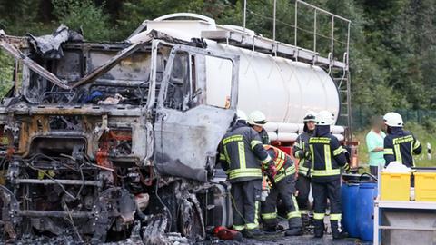 Ein ausgebrannter Lkw steht am Fahrbahnrand, Feuerwehrleute stehen dabeben