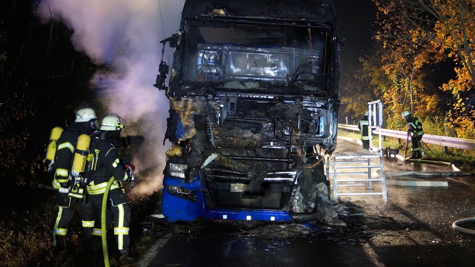 Feuerwehrleute löschen mit einem Schlauch einen rauchenden Lkw.