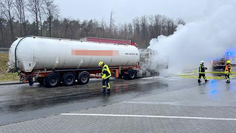 Foto: Rauch steigt aus einem Lkw auf, der auf auf einem Parkplatz steht. Daneben Feuerwehrleute.