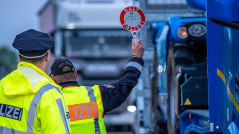 Polizist von hinten mit "Halt"-Schild vor Lkw