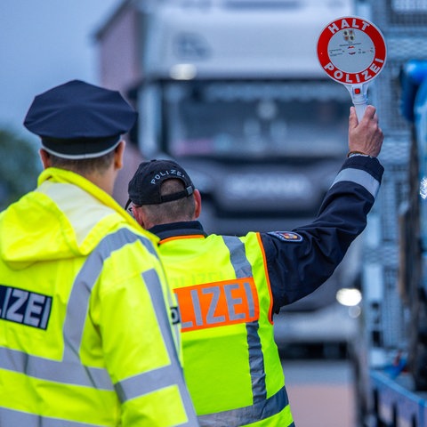 Polizist von hinten mit "Halt"-Schild vor Lkw