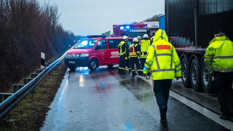 Polizisten und Feuerwehrleute in neon-gelber Arbeitskleidung auf der verregneten Autobahn neben einem Lkw, im Hintergrund zwei Feuerwehrwagen