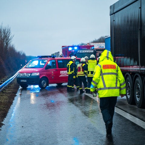 Polizisten und Feuerwehrleute in neon-gelber Arbeitskleidung auf der verregneten Autobahn neben einem Lkw, im Hintergrund zwei Feuerwehrwagen