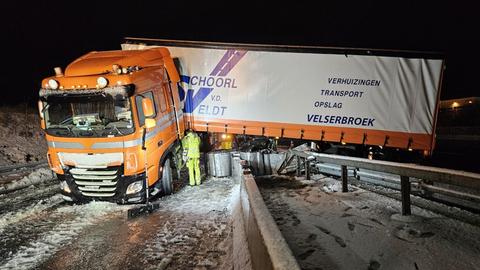 Sattelschlepper verkeilt auf Leitplanke, Schnee, Mann in gelber Kleidung