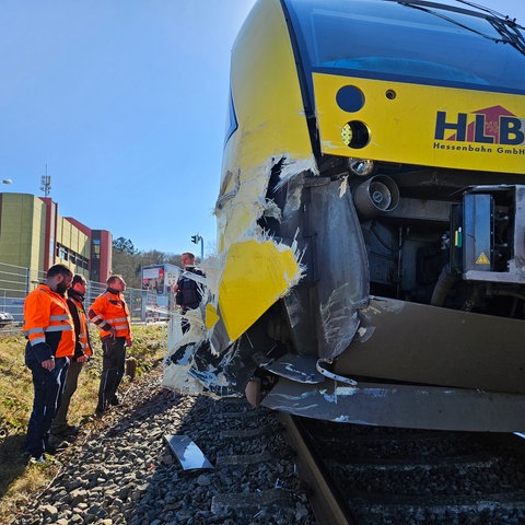 Arbeiter in Warnwesten stehen neben der beschädigten Regionalbahn.