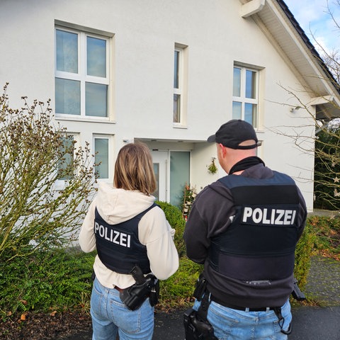 Zwei Polizeibeamte stehen vor einem weißen Wohnhaus in Löhnberg (Limburg-Weilburg)