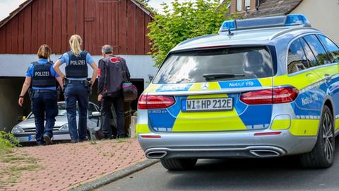 Polizisten stehen vor einem Haus mit Garage, in der ein Kleinwagen steht