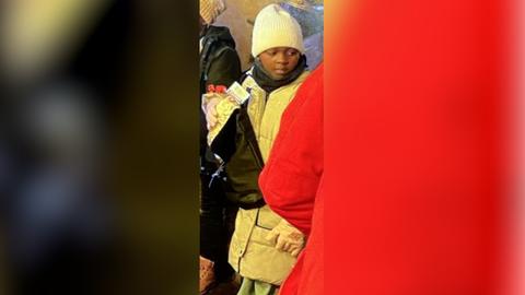 Bild von vermisster Neunjähriger aus Uganda: Mädchen im beigen Mantel und weißer Mütze steht in Gruppe. Bild auf Frankfurter Weihnachtsmarkt aufgenommen.