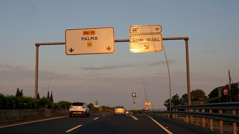 Auf einer Autobahn hängen Schilder mit der Aufschrift "Palma" und "Son Gual", darunter fahren Autos.